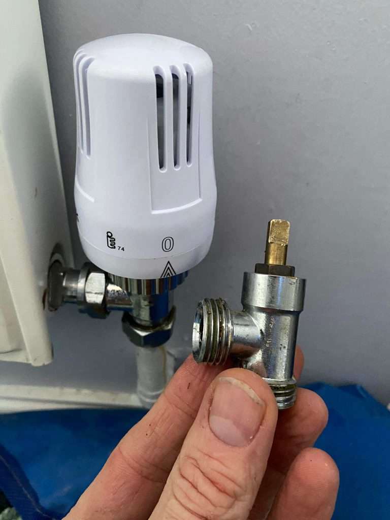 a hand holding a metal lockshield valve and a trv on a radiator